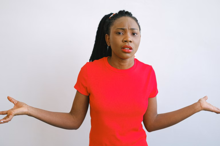 Young black woman in a red shirt with a confused expression. Perfect for emotive stock photo needs.